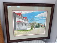 Framed watercolor painting showing a landscape with a large white house with red roof, road, hills, church steeple, and blue sky with clouds, signed by LS Wolfs.