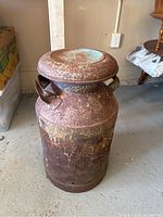 Full view of the rusted metal milk can standing on a floor, showing overall condition and shape