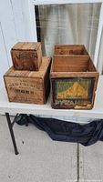 Overview of three wooden crates on table outside with branding on sides, showing size and condition
