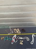 Photo of assorted necklaces laid out on a black surface with measuring tape for scale, showing variety of bead colors and sizes.