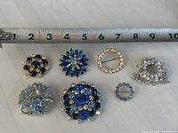 Seven vintage rhinestone brooches displayed with measuring tape showing sizes.