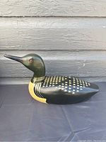 Full side view of wooden duck decoy showing painted black and cream color with patterned feathers.