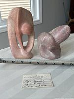 Two soapstone sculptures side by side with certificate tag and measuring tape laid horizontally in front
