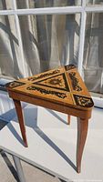 Side view of triangular wooden side table showing detailed floral and geometric inlay on the top lid.