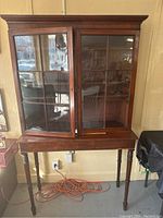 Overall front view of the two piece wooden display cabinet showing glass paneled doors and lower stand with legs