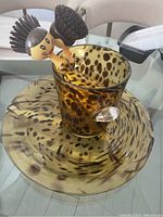 Photo of large round decorative cheetah print dish with matching glass vase containing two character kitchen brushes with yellow handles and round bristle heads.