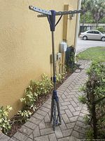 Foldable tripod clothes dryer set up outdoors on a brick pathway, showing the drying arms and tripod legs.