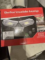 Front and top of red box featuring product name, images of the deformable lamp, and lighting specification details including 8000 lumens and retrofit light designation.