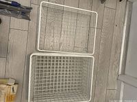 Photo showing two white wire baskets stacked inside each other on a wood floor.