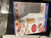 Bonjour Cookie Factory box front showing images of cookies made with the press and description of its press-and-release operation with three interchangeable cookie shapes.