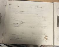 Top view of a distressed white wooden stove noodle board cover showing wood grain and brush marks with two brushed nickel handles partly visible on either side.