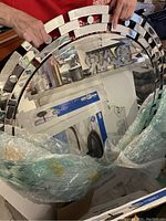 Full view of the large decorative round mirror showing reflective glass segments and black backing, wrapped in bubble wrap for protection.