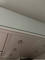 Close-up image showing part of the white dresser with two drawers and ring pull handles, and glass or mirror panel top surface reflecting the ceiling.