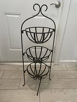 Full view of the black wrought iron three-tier fruit basket stand showing design, structure, and condition.