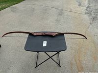 Full view of the vintage wooden recurve bow laid flat on a black folding table outdoors, showing the bow's shape and finish.