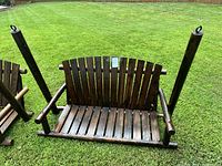 Front view of a solid wood outdoor swing seat with slatted back and seat, armrests, standing on grass.