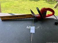 Photo showing side view of the Homelite HedgeSweep electric hedge clippers with wooden blade cover and red and black handle.