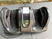 Black electric foot massager with two fabric-lined foot compartments and central control panel.