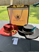 Two hats displayed on a table outside with Fruition Hat Co. branded bag behind them.
