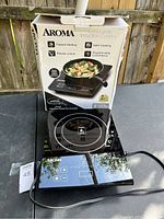 Photo of induction cooktop and its original box showing product features like fastest heating, safer cooking, precise control, programmable convenience, and included pan.