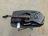 Black Mitchell electric guitar lying on top of a black soft gig bag on a small table outdoors.