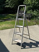 Photo of a 4-foot aluminum platform ladder with four steps and a broken paint shelf area. Ladder placed on concrete outdoors.