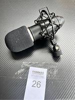 Full view of black microphone with foam windscreen and shock mount on a carbon fiber textured background, with MaxSold lot tag visible.