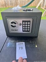 Front view of the First Alert safe showing keypad, key slot, and keys on top along with mounting bolts in plastic bag