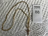 Full view of gold plated cross pendant necklace with chain on textured white surface.