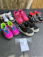 Six pairs of toddler shoes displayed on a black table, showing overall lot contents in natural light.
