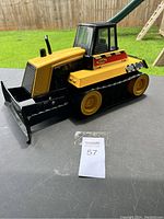 Full side view of yellow Tonka bulldozer truck on table outdoors with green grass background, showing front blade and track wheels