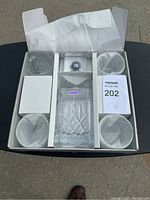 Boxed set showing the Waterford Marquis decanter with stopper in the center and four crystal glasses surrounding it, all protected by white tissue paper, in original packaging.