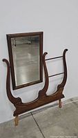 Front view of antique mirror with attached wooden stand, showing rectangular mirror and decorative wooden supports with curved details.