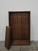 Front view of the empty wooden bookcase frame with three loose shelves placed inside the unit.