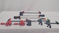 Full view of all clamps in the lot showing 2 pairs of bar clamps, orange corner angle clamps, and hold clamps