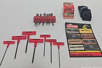 Red-handled Craftsman hex wrenches and other tool items laid out, including adjustable hole saw with black case and spade bit set in box.