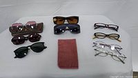 Full view of all eyeglasses and sunglasses laid out, showing 9 glasses in total and a brown fabric case.