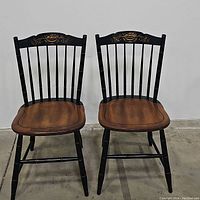 Pair of chairs front view showing black frame, gold floral motif, brown seats