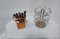 Photo showing wooden butcher block with seven black-handled knives and metal Keurig K-Cup pod carousel stand on white background.