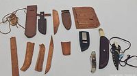Full assortment of leather sheaths, parts and cutting tools displayed on a white surface
