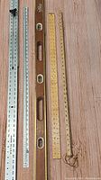 Full set showing two metal rulers, two wooden measuring sticks, and one wooden level on wood background.