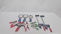 Overview of assorted metal clamps in the lot including various spring clamps and plier style clamps with red, black, and green handles
