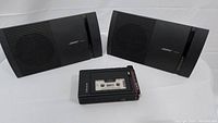 Pair of Bose Model 100 speakers and vintage Sony cassette player on white background