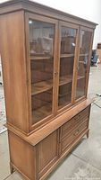 Front angled view of solid oak china hutch showing three glass doors, brass hardware, and tapered legs.