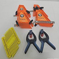 Photo showing two orange Rockler Feather-Loc bandy clamps, four yellow plastic feather-loc bench dogs, and two black and blue spring clamps.