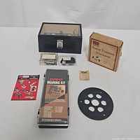 Overall lot overview showing black wooden case with router bits, Porter-Cable router trimming attachment box, router bit bearing kit, and small accessory boxes