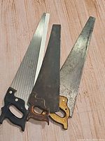 Three handheld wood cutting saws on wood surface, showing handles and blades