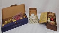 Three boxes containing vintage Christmas ornaments including colorful glass baubles, gold glitter ornaments, and crystal decorations