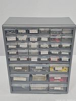 Front view of gray plastic storage unit with many clear drawers filled with assorted hardware items, each labeled.