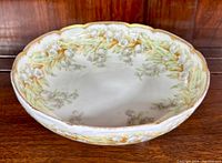 Top view of the round Limoges trinket bowl with raised white floral motifs and soft green and beige glaze.